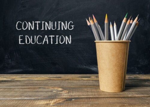 A wooden table with a brown cup of pencils and chalkboard with the words Continuing Education written on it